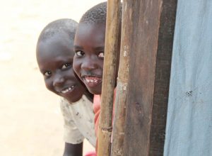 2 children peep round corner at Palabek refugee settlement